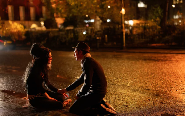 HD desktop wallpaper featuring a scene from the movie Back to Black, depicting Amy Winehouse and a man sitting on a dimly lit street at night.