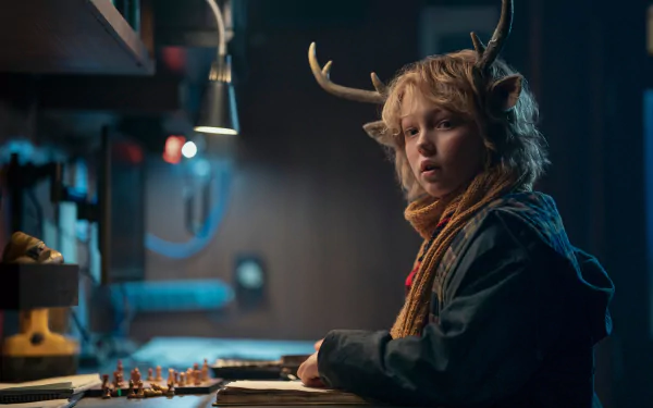 HD wallpaper of Gus (Sweet Tooth), portrayed by Christian Convery in the TV show Sweet Tooth, features a boy with antlers sitting at a desk in a dimly lit room.