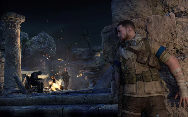 A high-definition desktop wallpaper and background from the video game Sniper Elite III, showing a soldier in tactical gear hiding behind ancient ruins, observing enemies by a campfire at night.