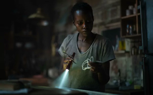 HD desktop wallpaper from A Quiet Place: Day One featuring Lupita Nyong'o in a dimly lit scene, holding a flashlight and string, highlighting the suspenseful atmosphere of the movie.