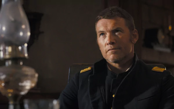 HD wallpaper featuring Sam Worthington in character from the movie Horizon: An American Saga - Chapter 1, seated and wearing a dark uniform with yellow insignia.
