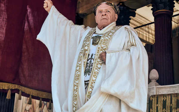Anthony Hopkins in character from the TV show Those About to Die, dressed in elaborate ancient attire, arm raised, set as an HD desktop wallpaper and background.