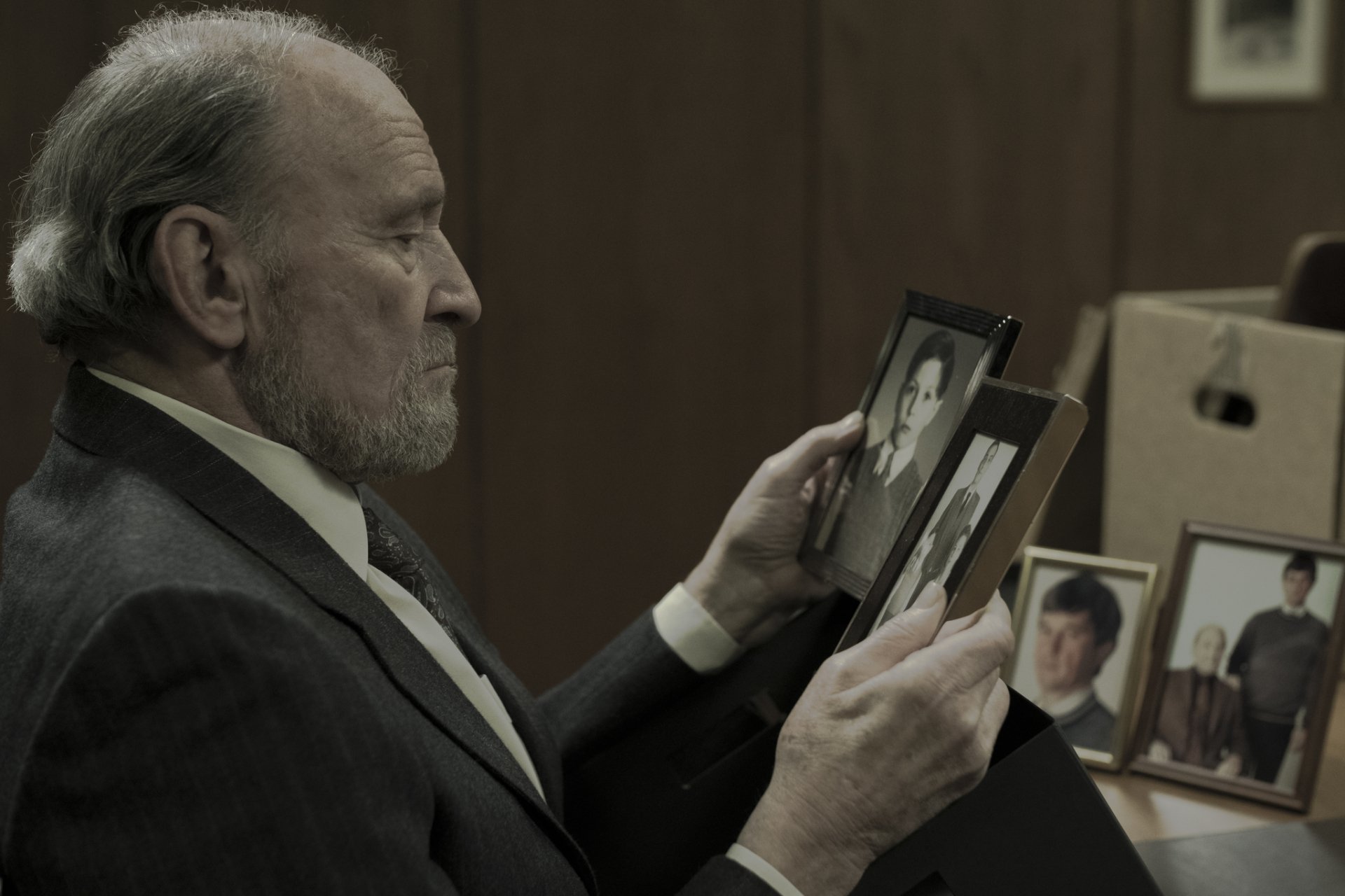 A man in a suit gazes thoughtfully at old photographs, creating a poignant atmosphere reminiscent of the dark themes explored in the TV show Dark. HD desktop wallpaper.