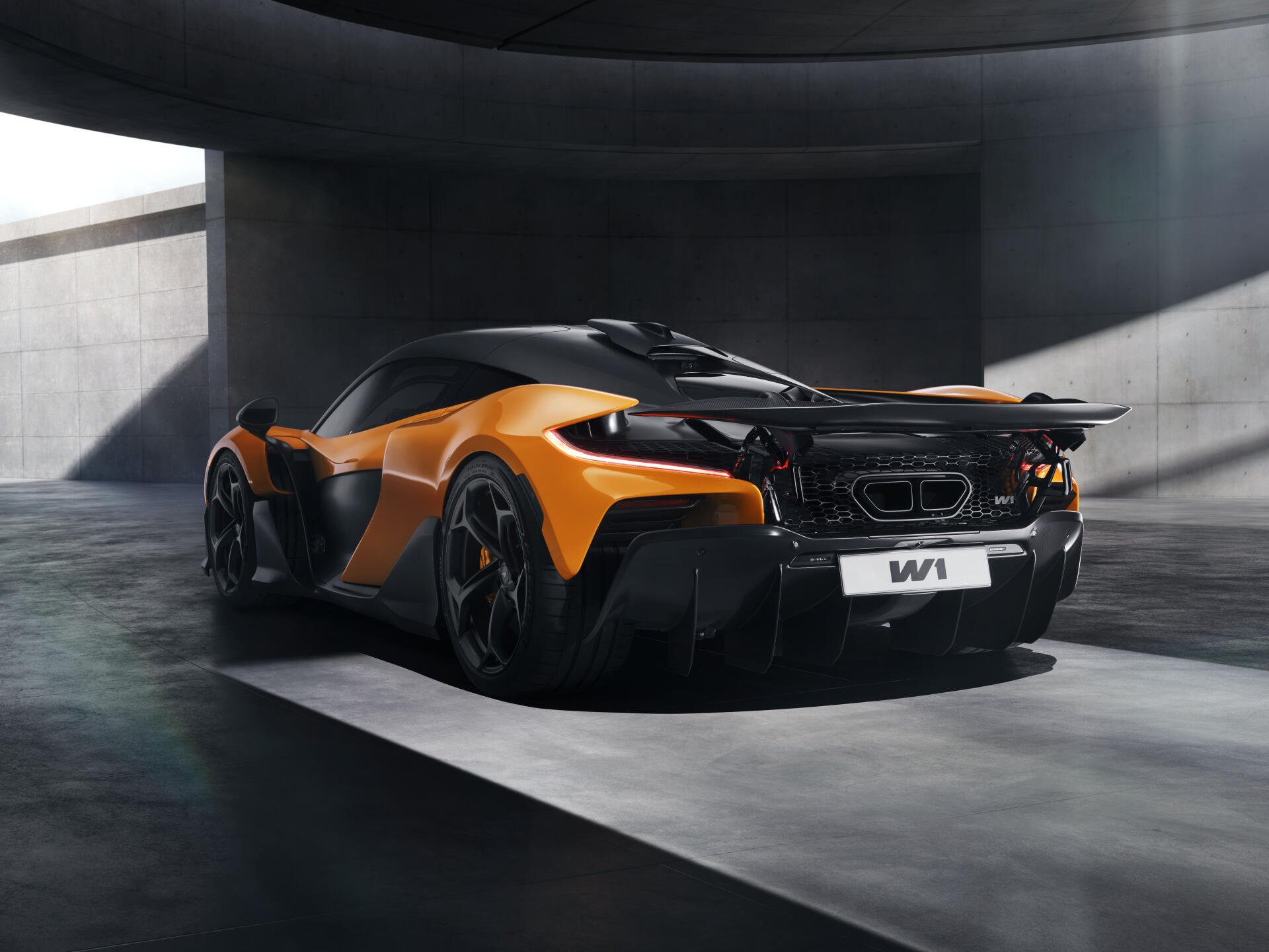 A stunning McLaren W1 in vibrant orange and sleek black, showcased in an architectural setting. This 8K Ultra HD image serves as an impressive desktop wallpaper.