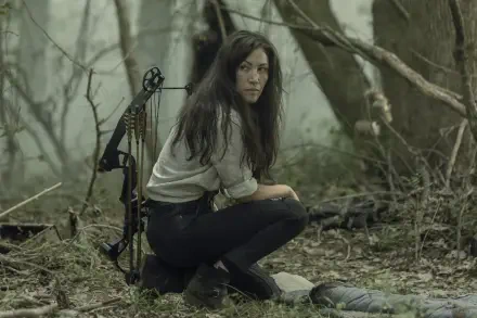 Eleanor Matsuura portrays a survivor in The Walking Dead, crouching in a dense, eerie forest, bow nearby, capturing the tense atmosphere of the show. HD wallpaper for fans.