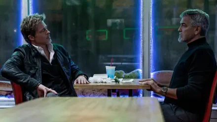 George Clooney and Brad Pitt engage in a tense conversation in a vibrant, neon-lit setting from the movie Wolfs (2024). This HD wallpaper showcases their dynamic interaction.