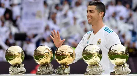 Cristiano Ronaldo, in a Real Madrid C.F. kit, smiles and waves while standing beside five Ballon d'Or trophies in this dynamic HD sports wallpaper.