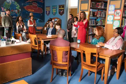 A vibrant scene from the TV show *Abbott Elementary*, featuring a diverse group of characters gathered in a classroom, engaged in discussion around wooden tables, with bookshelves in the background.