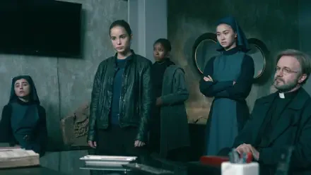 A scene from the TV show Warrior Nun, featuring Alba Baptista and fellow cast members in a tense gathering, set against a modern, minimalistic background.