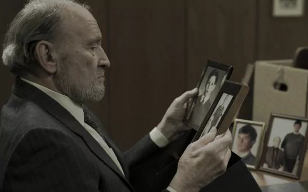 A man in a suit gazes thoughtfully at old photographs, creating a poignant atmosphere reminiscent of the dark themes explored in the TV show Dark. HD desktop wallpaper.