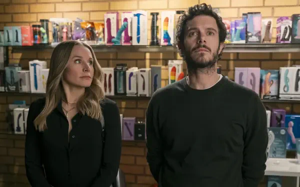 Kristen Bell and Adam Brody stand in a shop filled with colorful products in a scene from the TV show Nobody Wants This. The image serves as a vibrant HD desktop wallpaper.