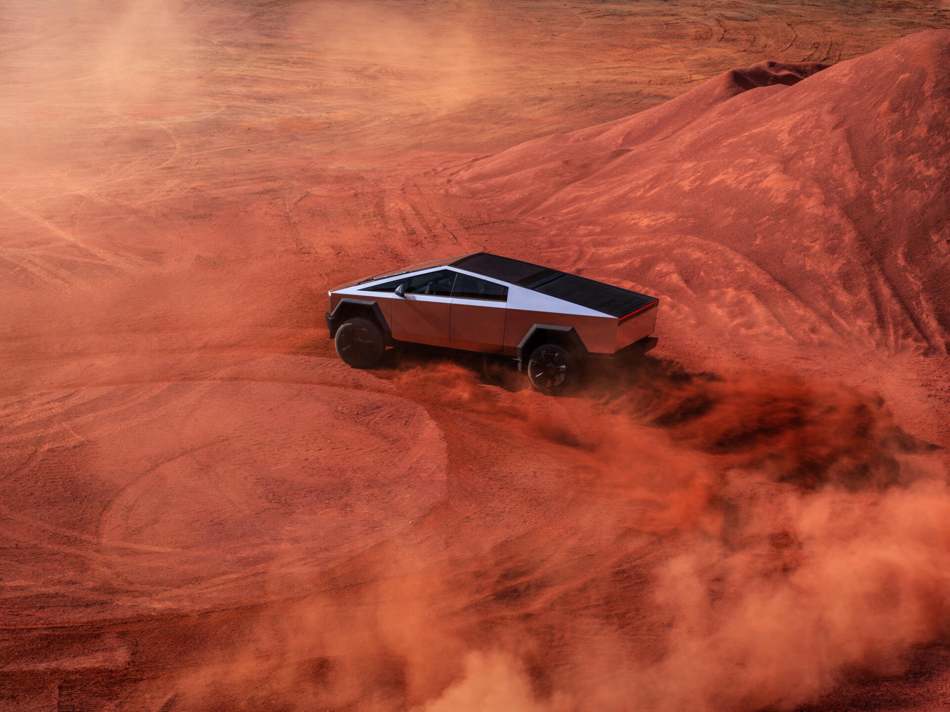 A Tesla Cybertruck maneuvers through a rugged, red landscape, capturing an adventurous spirit in this stunning 4K Ultra HD desktop wallpaper.