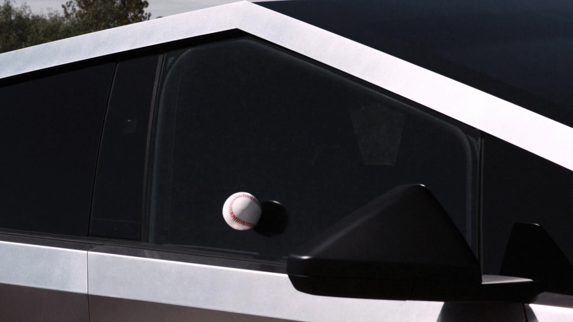 A close-up of a Tesla Cybertruck's angular design, featuring a baseball stuck against its dark window, showcasing the vehicle's unique style in this 4K Ultra HD desktop wallpaper.