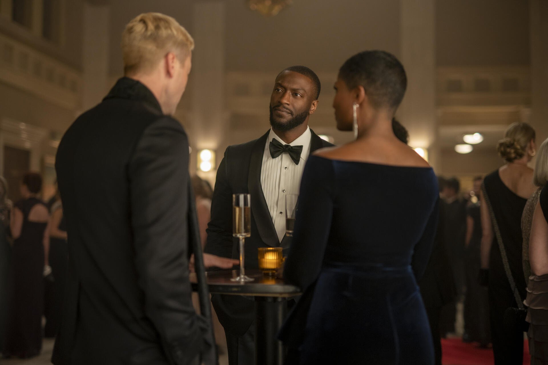 Aldis Hodge appears in a sophisticated scene from the TV show Cross (2024), engaging in conversation at a formal event surrounded by elegantly dressed attendees.
