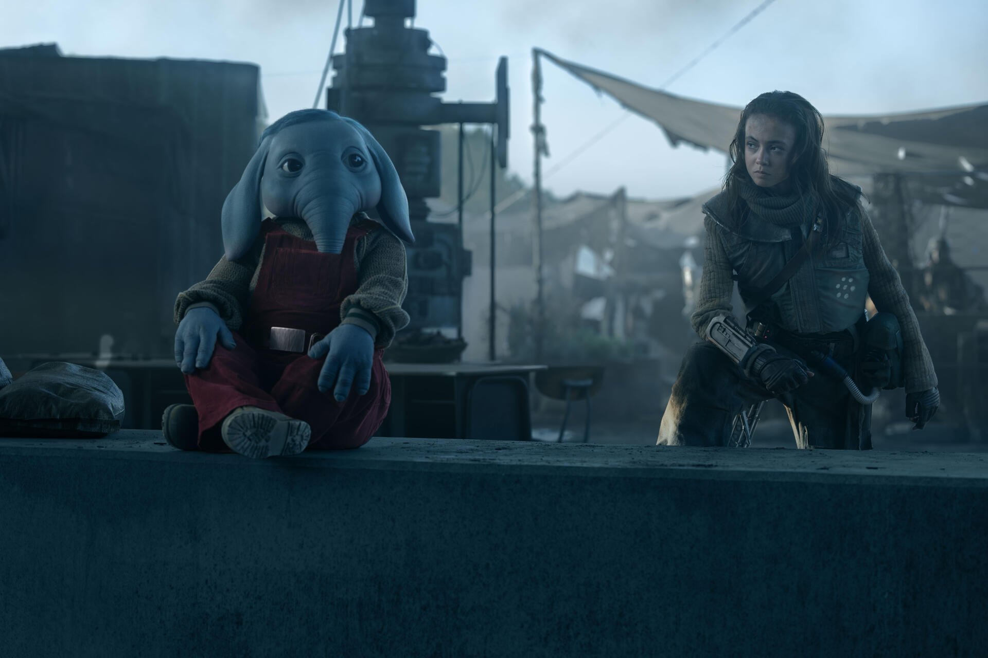 A scene from the TV show Star Wars: Skeleton Crew, featuring a unique character with blue skin and large ears sitting beside a companion in a mysterious setting. 4K Ultra HD wallpaper.