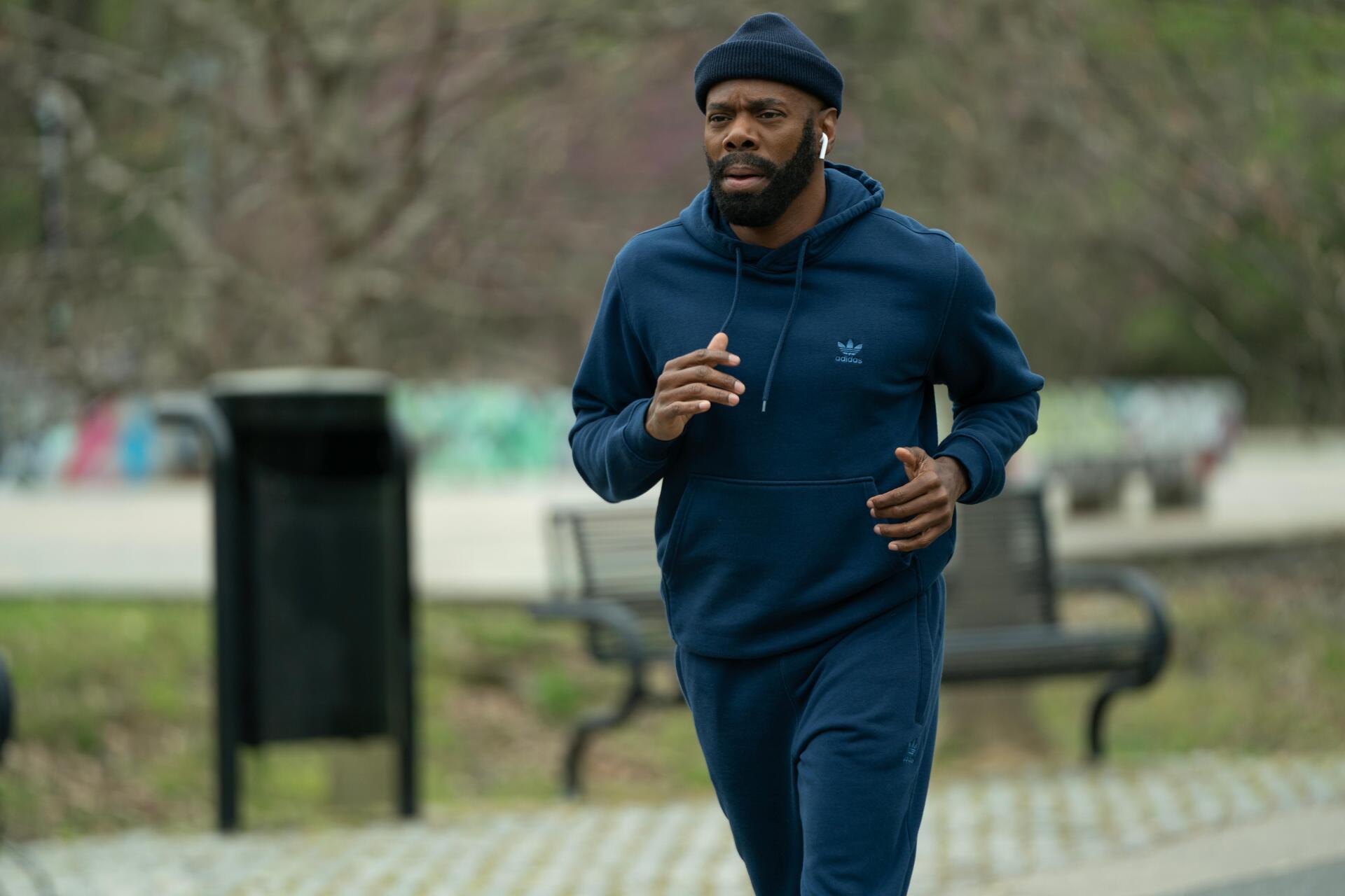 Colman Domingo jogs in a park, dressed in a blue tracksuit, from the TV show The Madness. This vibrant 4K Ultra HD wallpaper captures a dynamic moment in the series.