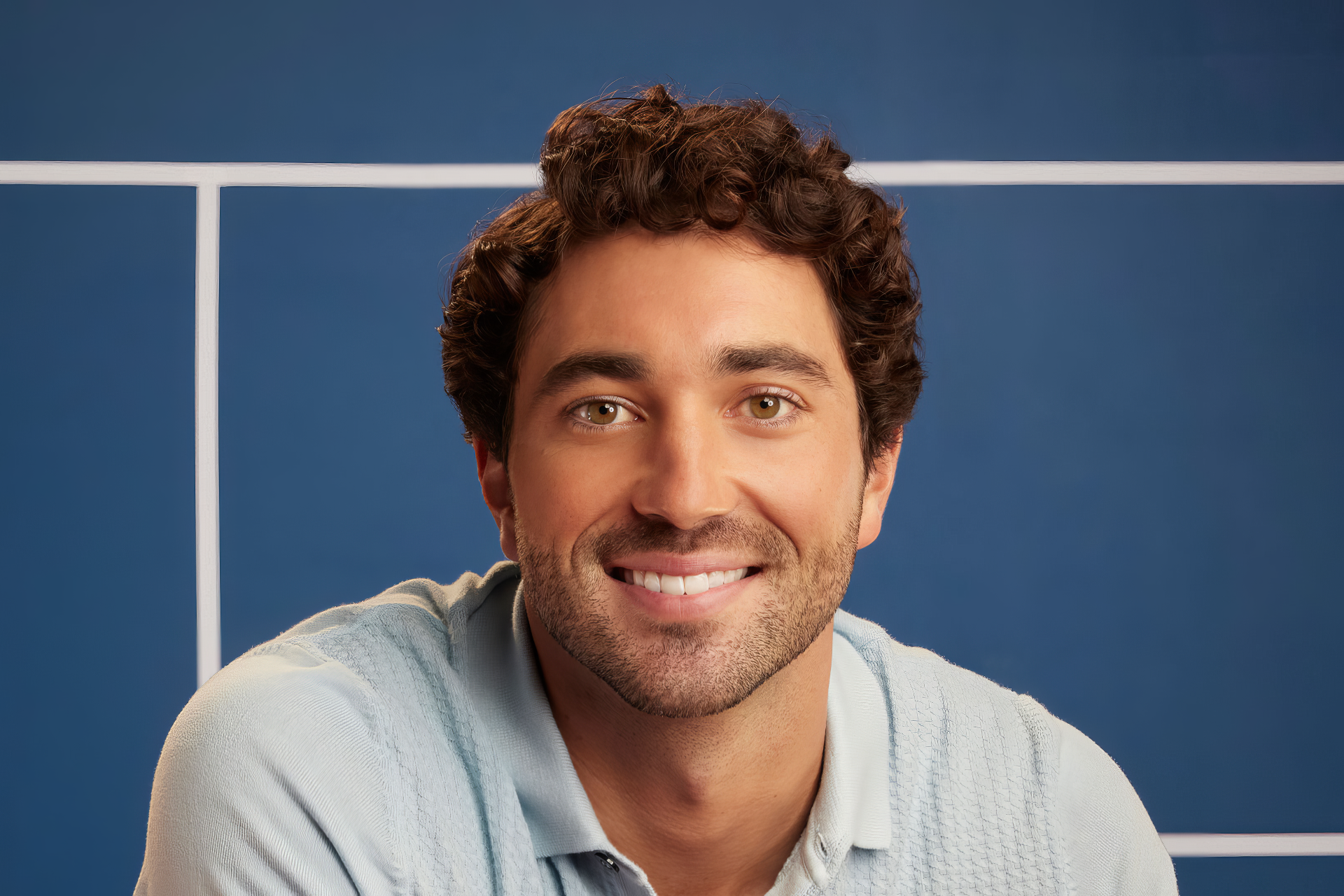 A high-definition desktop wallpaper featuring celebrity Joey Graziadei, smiling against a blue background, conveying a warm and approachable vibe.