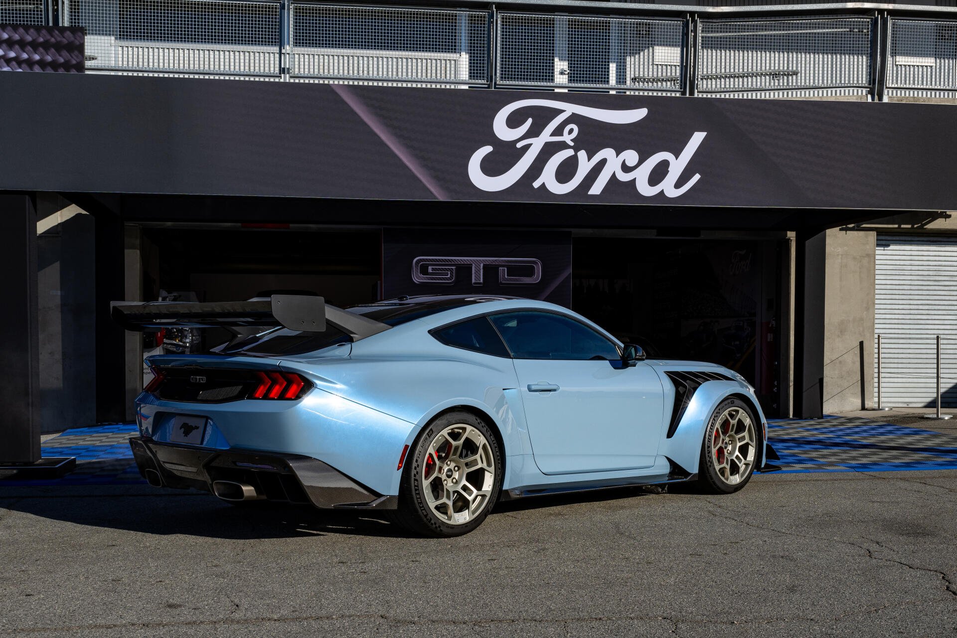 4K Ultra HD wallpaper showcasing a light blue Ford Mustang GTD parked outside a Ford dealership under a bold Ford logo sign.