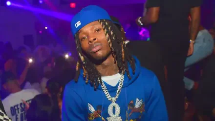 A vibrant HD wallpaper featuring rapper King Von, wearing a blue hoodie and cap, amidst a lively backdrop with club lights, capturing his dynamic presence in the music scene.
