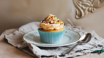 A beautifully decorated cupcake topped with colorful sprinkles, placed on a delicate plate, making for a charming 4K Ultra HD desktop wallpaper and background.
