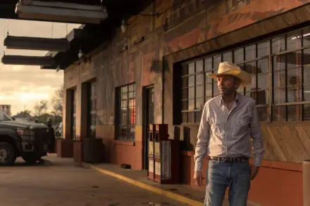 Billy Bob Thornton stands outside a rustic building in a scene from the TV show Landman. The image features warm, sunset lighting, creating an evocative backdrop.