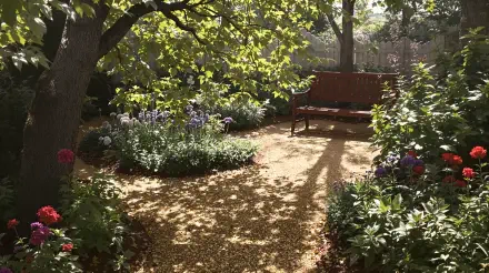 A tranquil cottagecore garden scene featuring lush greenery, colorful flowers, and a wooden bench, bathed in dappled sunlight, designed as a 4K Ultra HD desktop wallpaper.