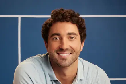 A high-definition desktop wallpaper featuring celebrity Joey Graziadei, smiling against a blue background, conveying a warm and approachable vibe.