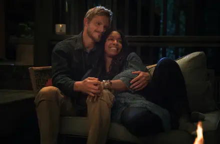 A cozy moment from the TV show Earth Abides, featuring Jessica Frances Dukes and Alexander Ludwig, captured in a warm, inviting setting.