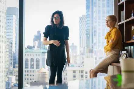 A scene from the movie Babygirl featuring Nicole Kidman, showcasing two women in a modern office with a city skyline in the background. 4K Ultra HD desktop wallpaper.