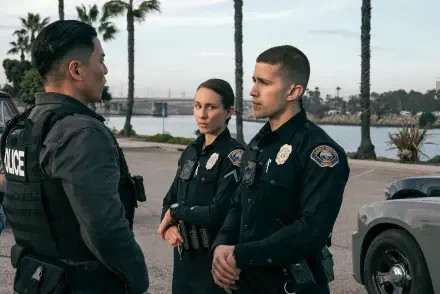 A scene from the TV show On Call (2025), featuring police officers engaged in conversation against a backdrop of palm trees and a serene water edge. 4K Ultra HD quality.