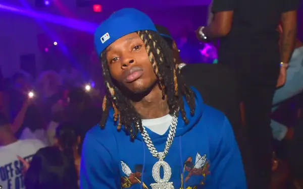 A vibrant HD wallpaper featuring rapper King Von, wearing a blue hoodie and cap, amidst a lively backdrop with club lights, capturing his dynamic presence in the music scene.