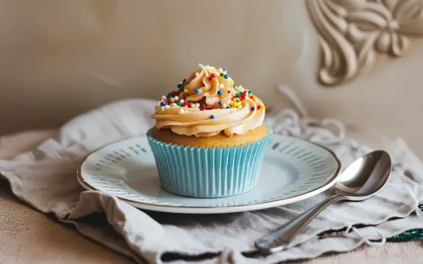 A beautifully decorated cupcake topped with colorful sprinkles, placed on a delicate plate, making for a charming 4K Ultra HD desktop wallpaper and background.