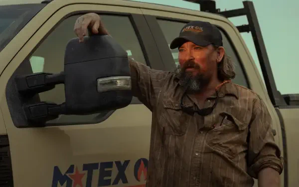 A rugged man leans against a truck, holding a mirror, set against an atmospheric backdrop from the TV show Landman. This image serves as a striking 4K Ultra HD desktop wallpaper.