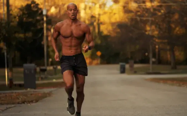 A muscular David Goggins runs through a park during autumn, showcasing determination and athleticism. This HD image serves as an inspiring desktop wallpaper for sports enthusiasts.