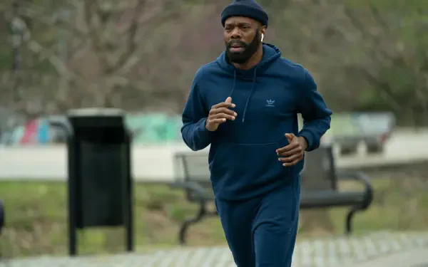 Colman Domingo jogs in a park, dressed in a blue tracksuit, from the TV show The Madness. This vibrant 4K Ultra HD wallpaper captures a dynamic moment in the series.