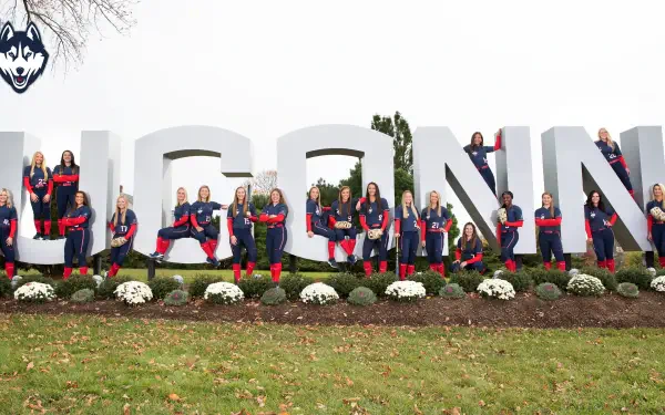 UConn Athletics team poses in front of large UConn signage, showcasing school spirit in a vibrant display. This HD wallpaper captures the pride and camaraderie of the athletes.