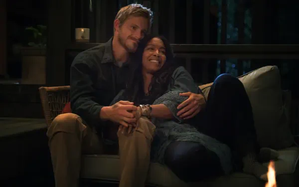 A cozy moment from the TV show Earth Abides, featuring Jessica Frances Dukes and Alexander Ludwig, captured in a warm, inviting setting.