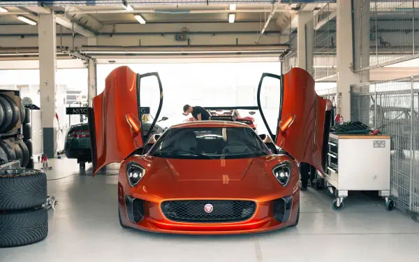 A striking Jaguar C-X75 luxury car with its distinctive doors open, set in a modern garage environment, showcasing its sleek design and performance-oriented features.
