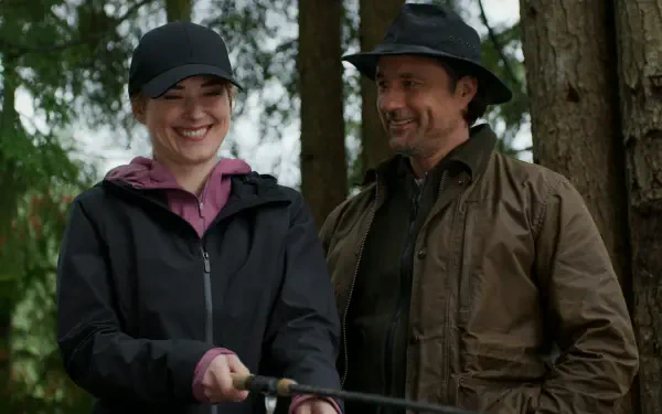 Scene from the TV show Virgin River (2019) featuring Martin Henderson and Alexandra Breckenridge. They share a joyful moment outdoors, surrounded by trees, enjoying nature together.
