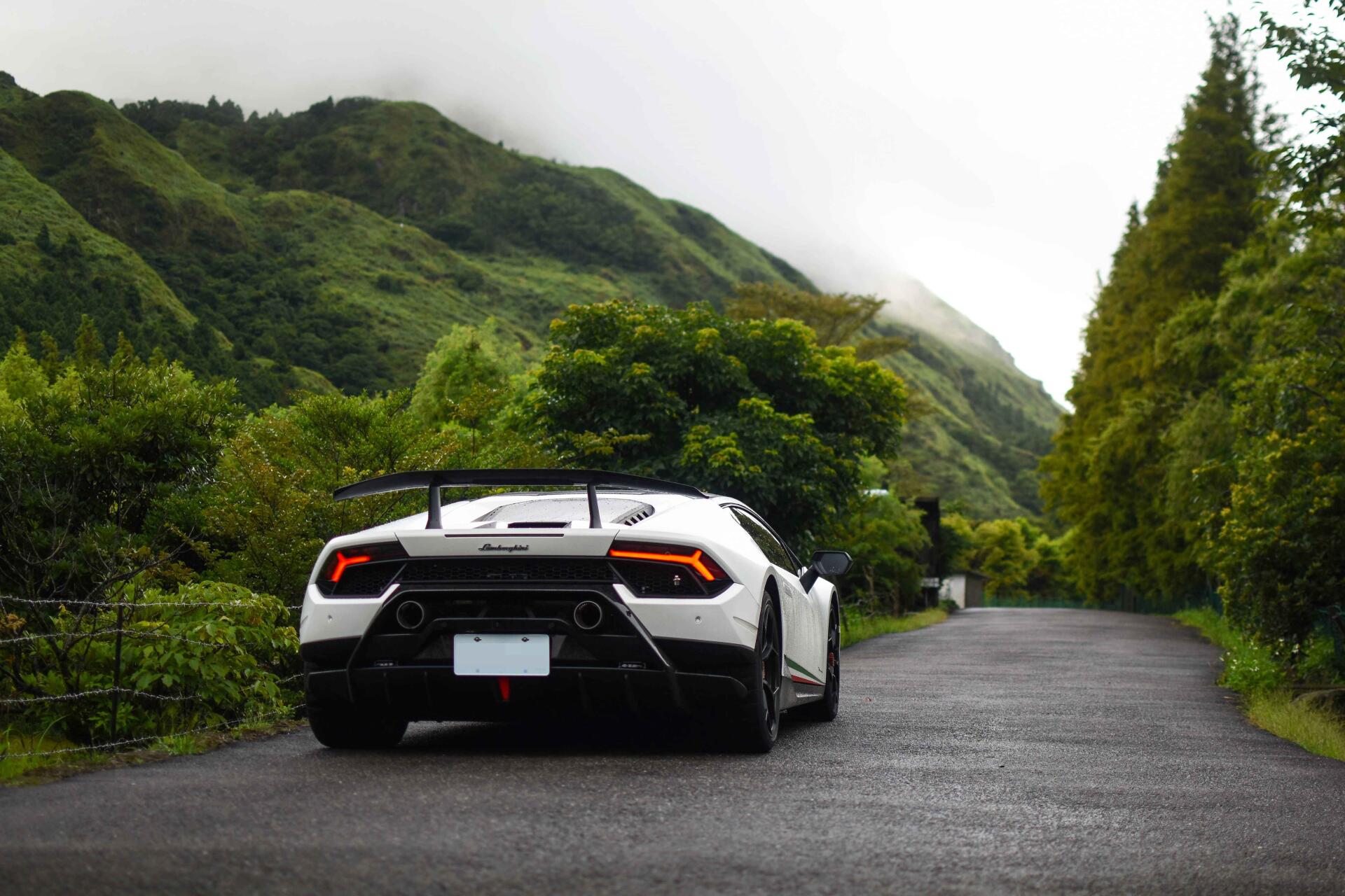 Rear view of a white Lamborghini Huracan sports car on a wet mountain road, surrounded by lush green hills — 5K Ultra HD PC desktop wallpaper/background.