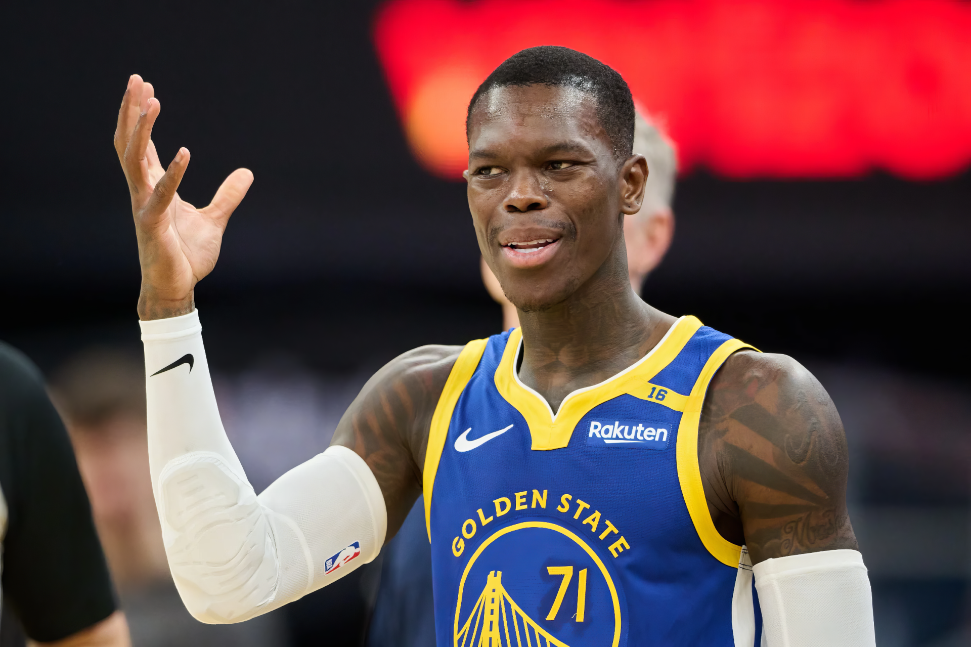 Dennis Schröder gestures playfully while wearing a Golden State Warriors jersey during an NBA game. This HD image captures the dynamic energy of basketball.