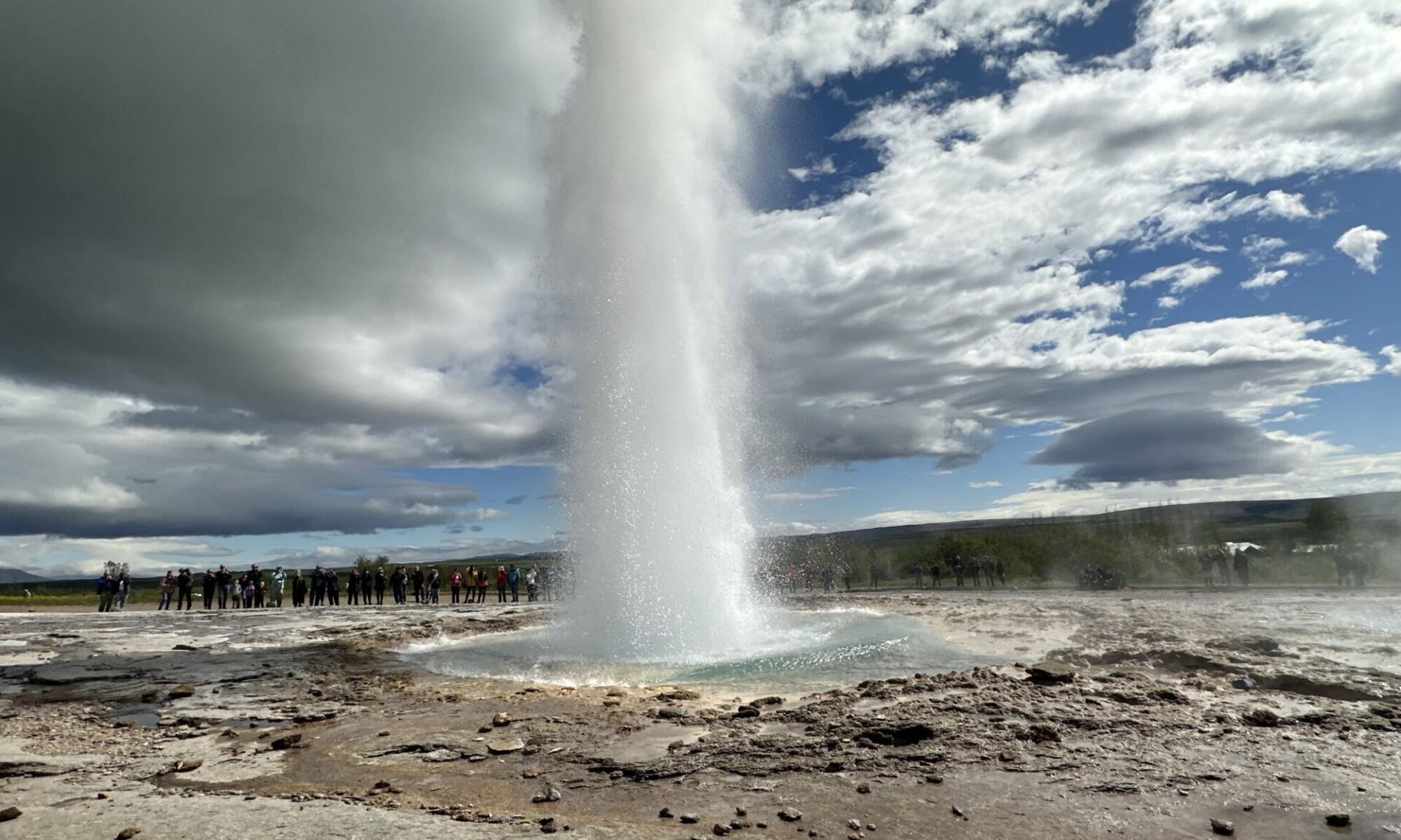 A powerful eruption of the Strokkur Geyser in Iceland shoots steam and water high into a partly cloudy sky, captured in HD for a desktop wallpaper background.