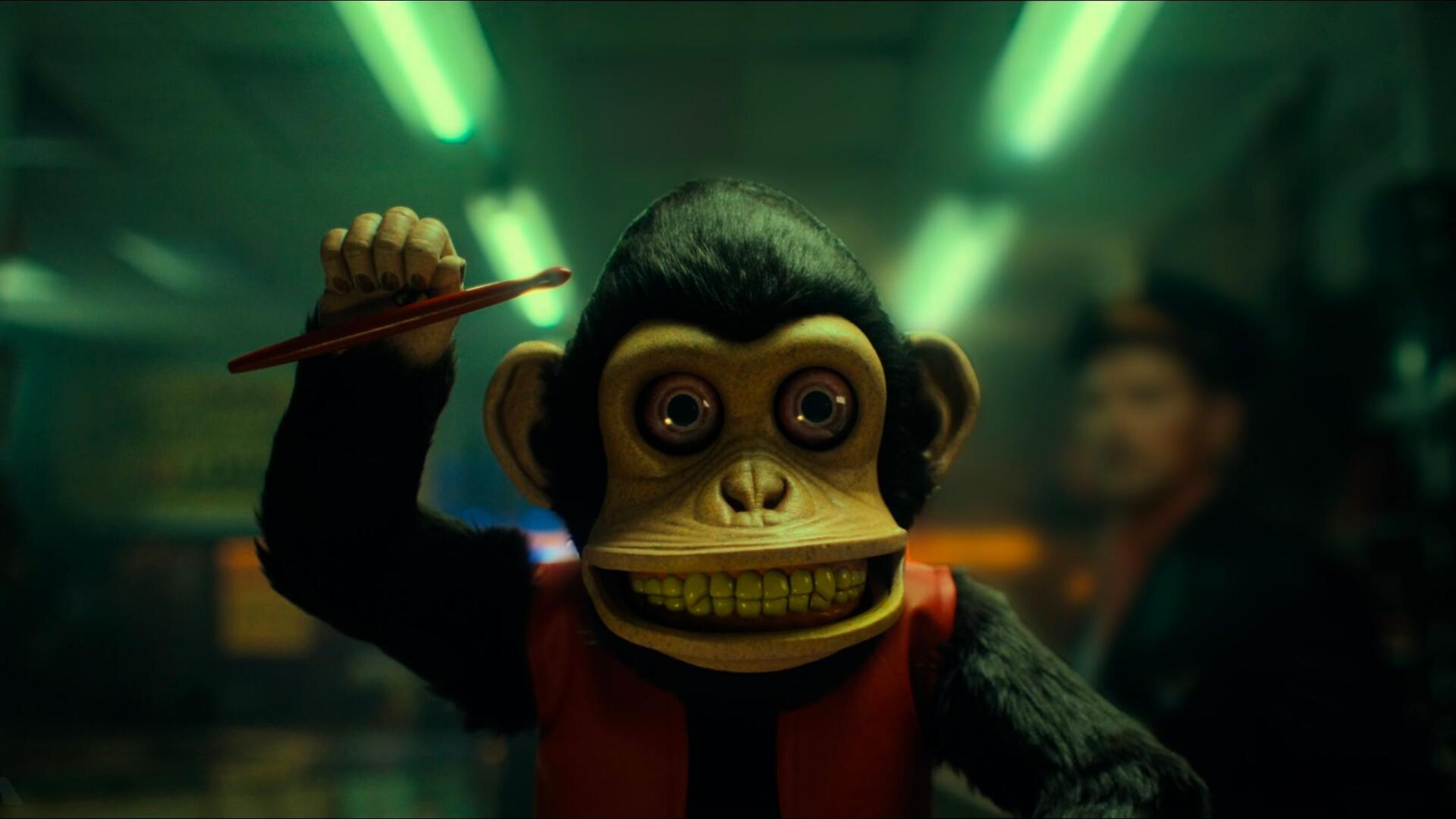 A vibrant HD wallpaper featuring a playful monkey character from the movie The Monkey (2025), set against an electrifying background with green lighting.