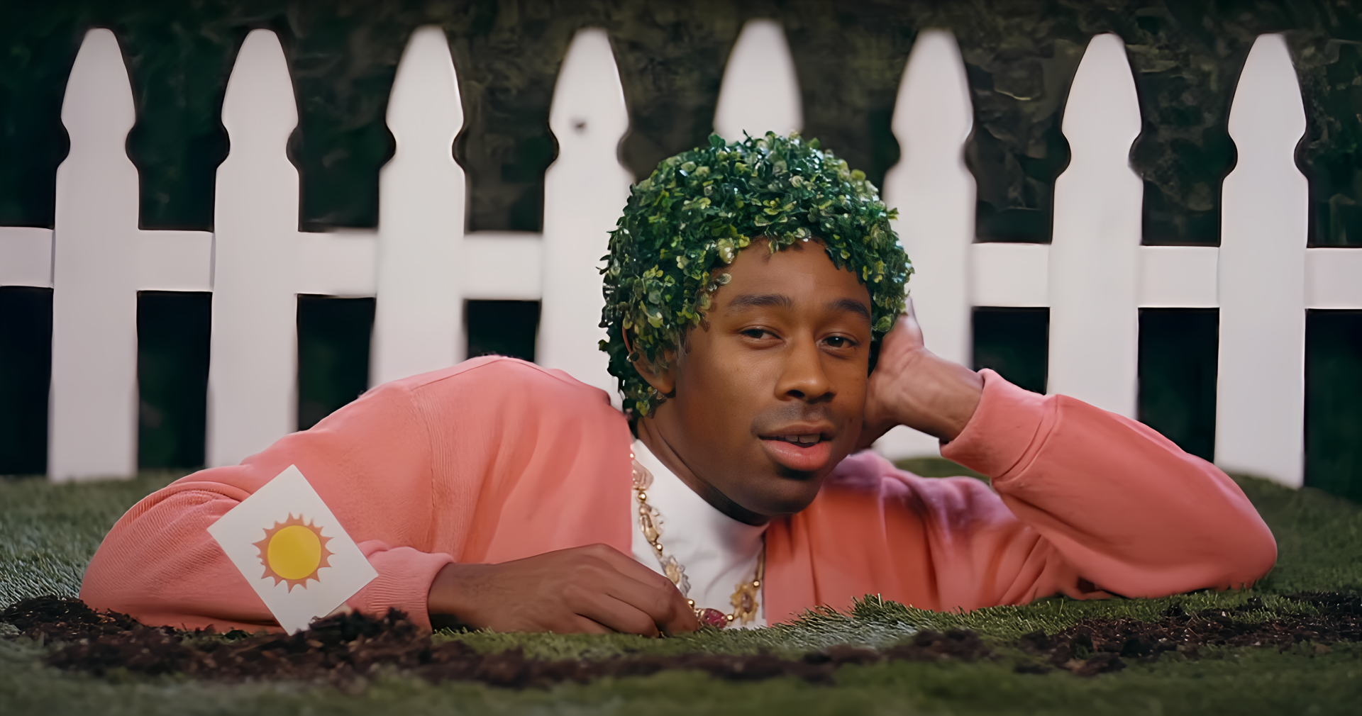 Person with green, foliage-style hair and pink cardigan lounging by a white picket fence — vibrant 2K Quad HD PC desktop wallpaper.