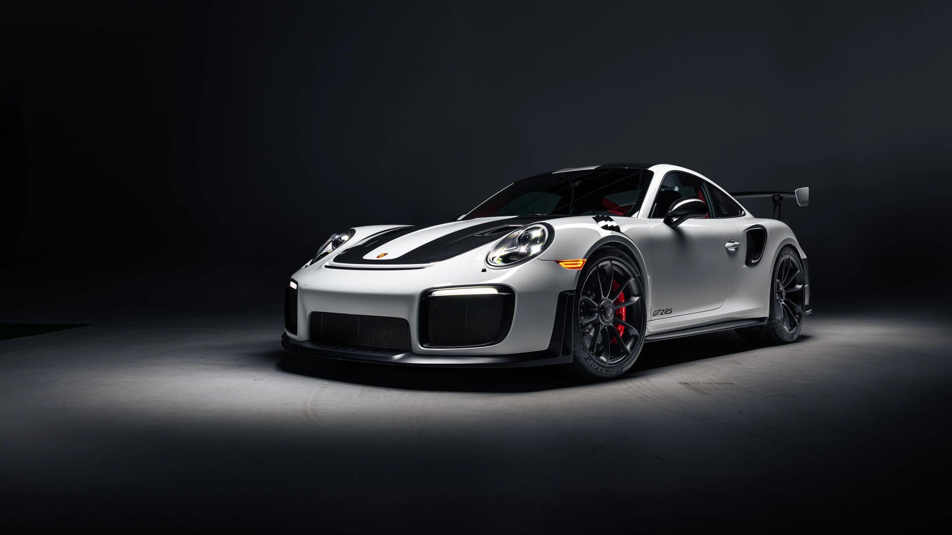 A sleek silver Porsche 911 GT2 RS Weissach is showcased against a dark backdrop, highlighting its aggressive design and performance features in stunning 8K Ultra HD quality.