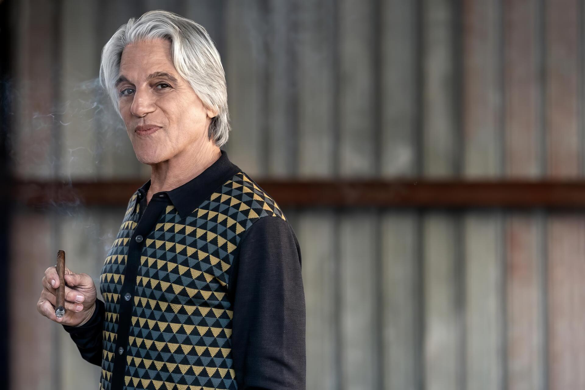 A character from the TV show Power Book III: Raising Kanan poses confidently, wearing a patterned vest, with a subtle smile against a textured backdrop. HD desktop wallpaper.