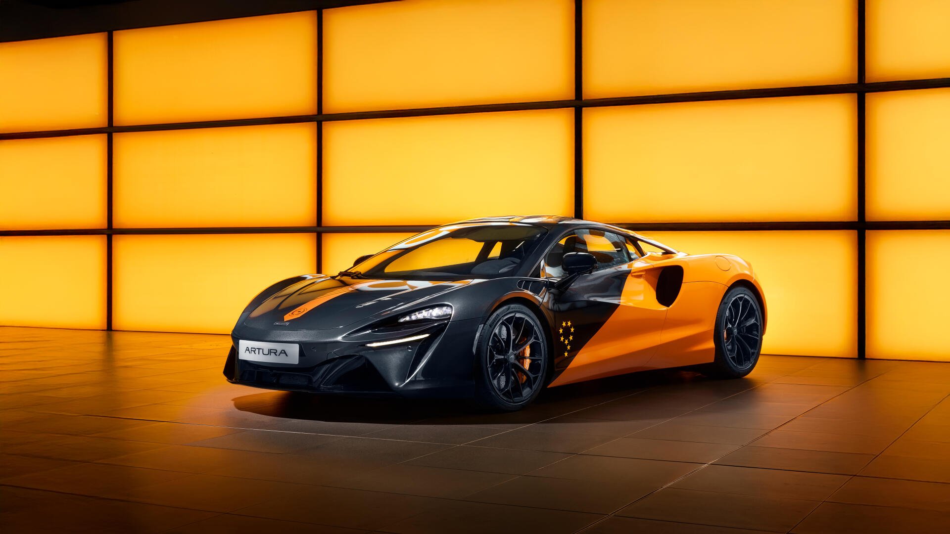 A sleek yellow and black McLaren Artura sports car showcased against a glowing orange grid backdrop. 4K Ultra HD PC desktop wallpaper and background.