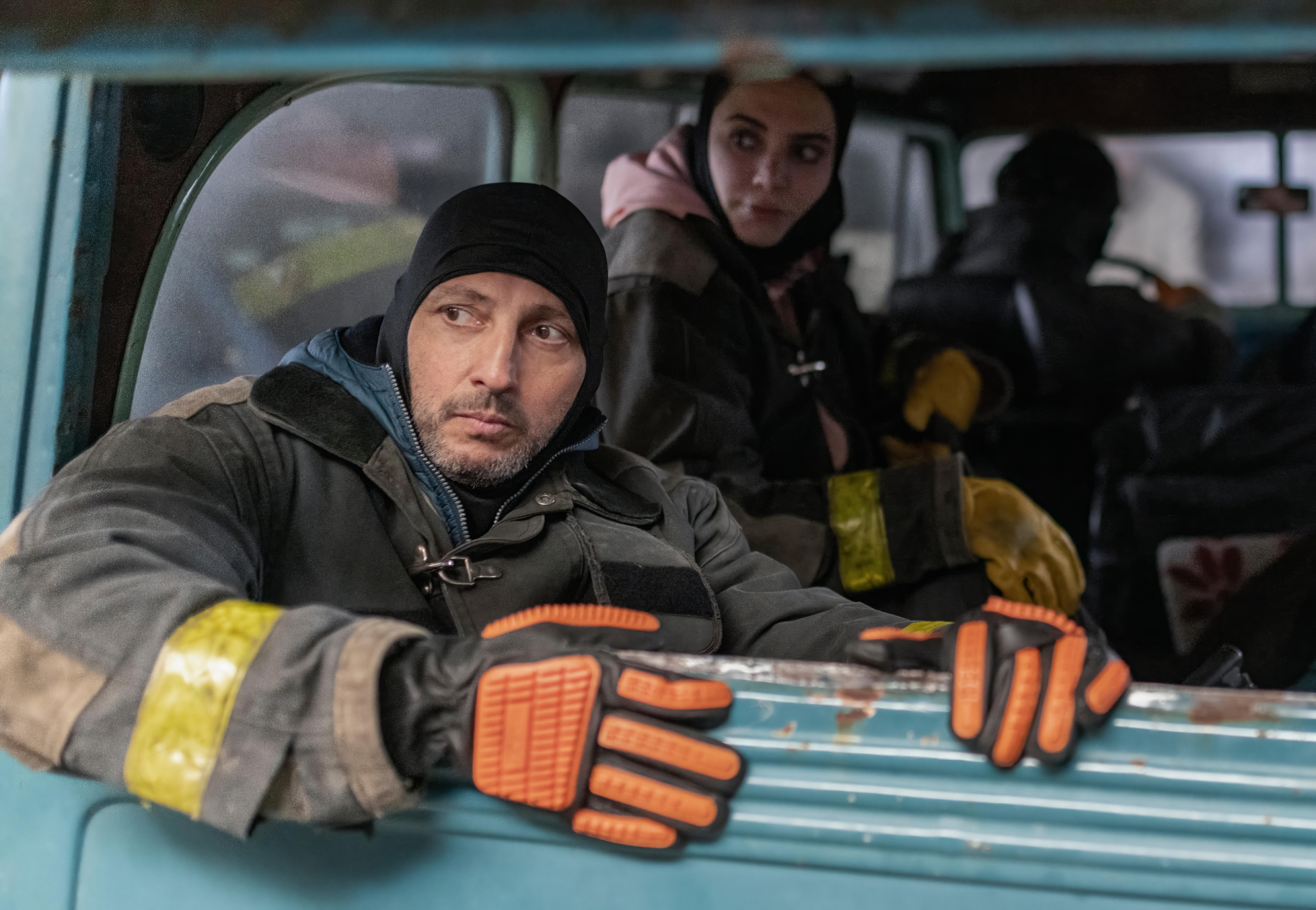 Scene from the TV show The Eternaut featuring characters in firefighter gear inside a vehicle, used as an HD PC desktop wallpaper and background.