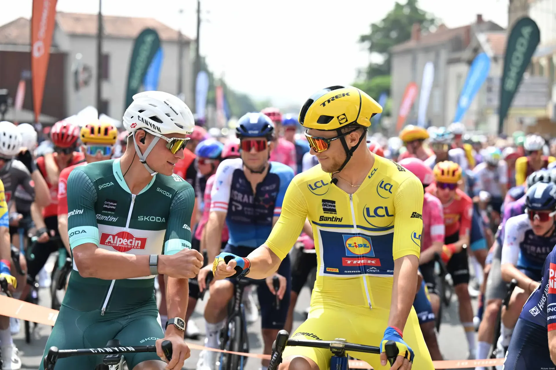 Cyclists in colorful gear exchange fist bumps during the Critérium du Dauphiné, captured in vibrant 4K Ultra HD for a dynamic sports desktop wallpaper.