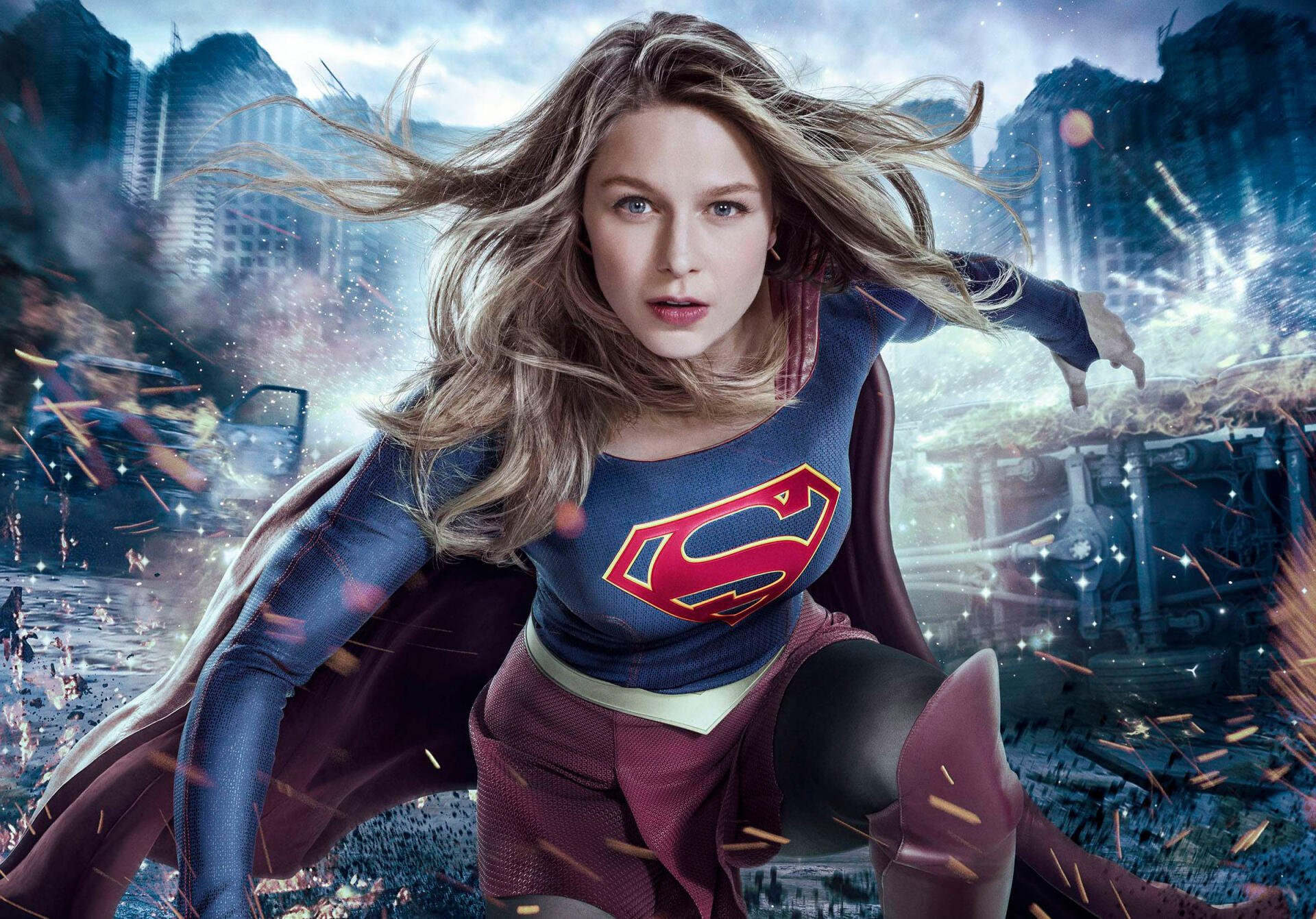 HD PC desktop wallpaper featuring Supergirl from the TV show, depicted flying confidently in her iconic suit with a cityscape background.
